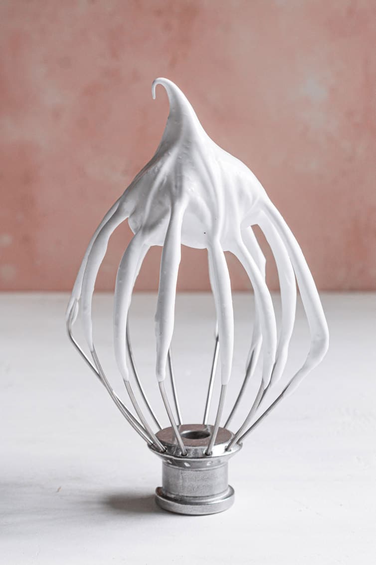 A whisk attachment with meringue on it, standing up on its own.