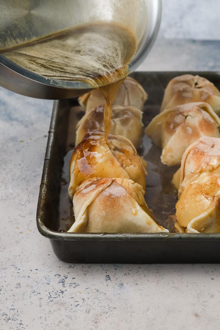 Pouring butter-brown sugar sauce over prepped apple dumplings.