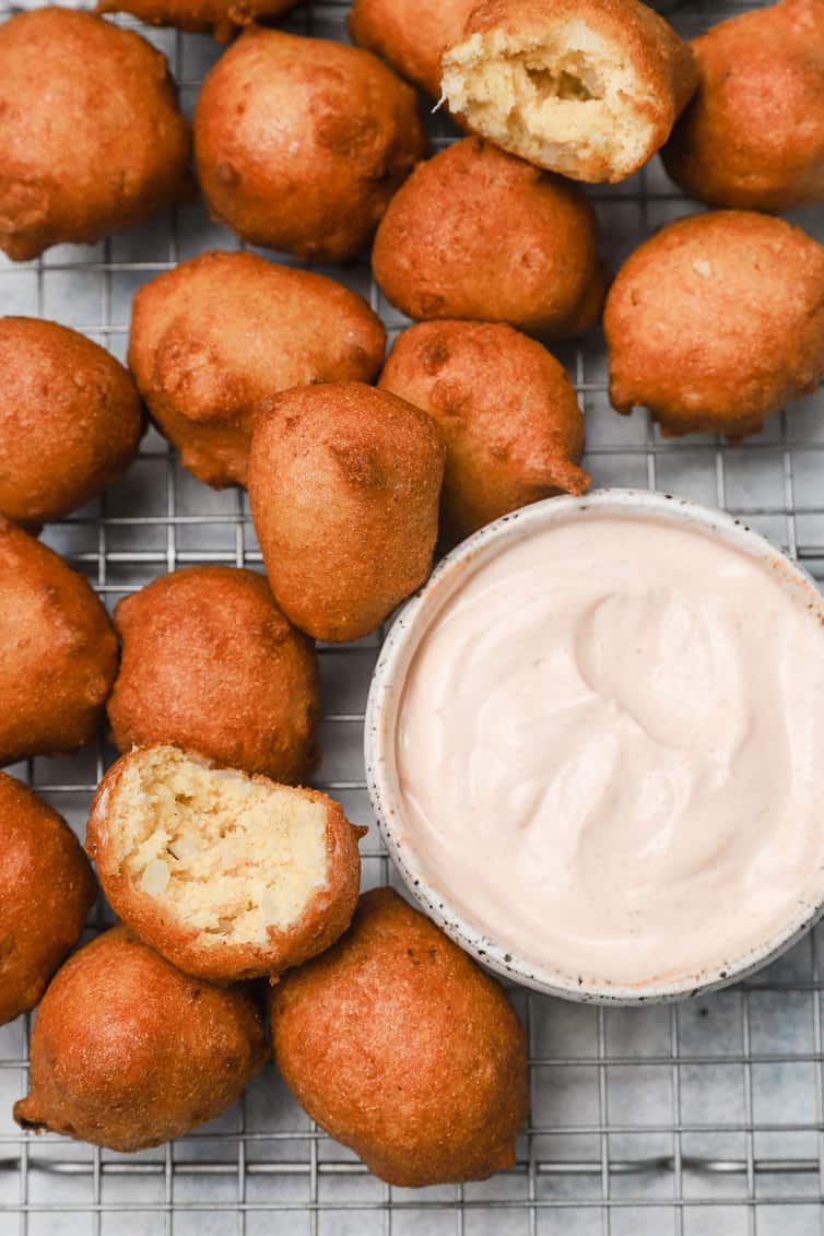Hush puppies on wire rack with bowl of dipping sauce.