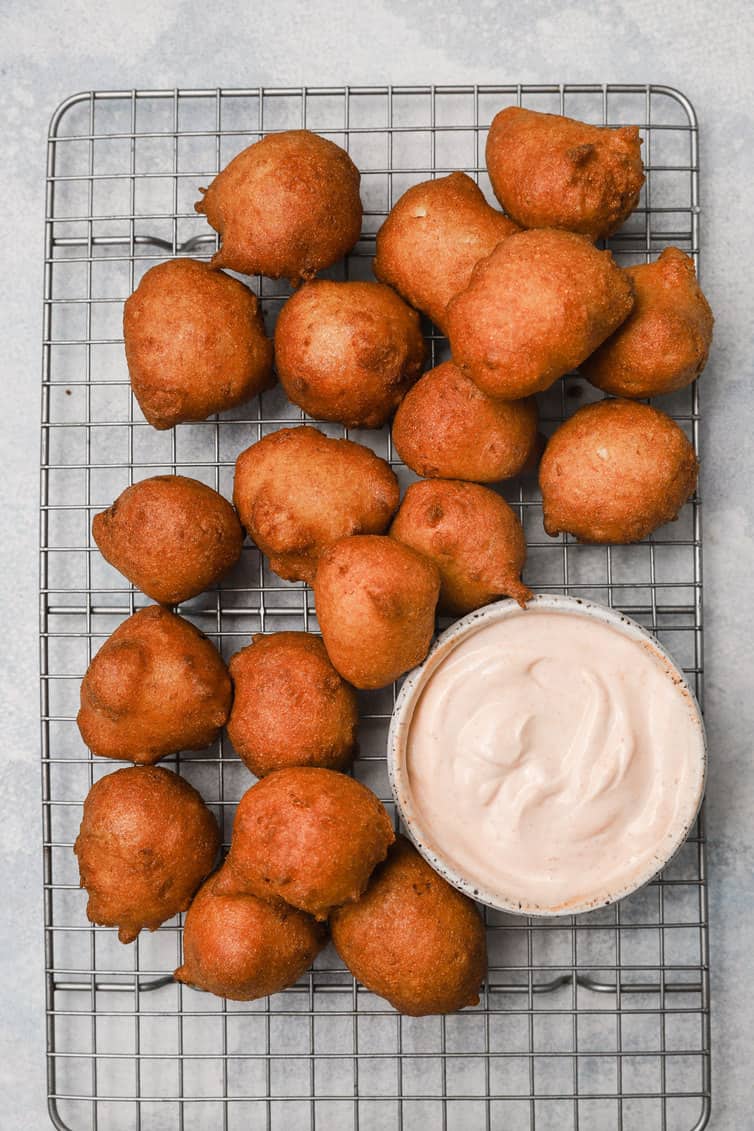 Hush puppies on cooling rack with bowl of dipping sauce.