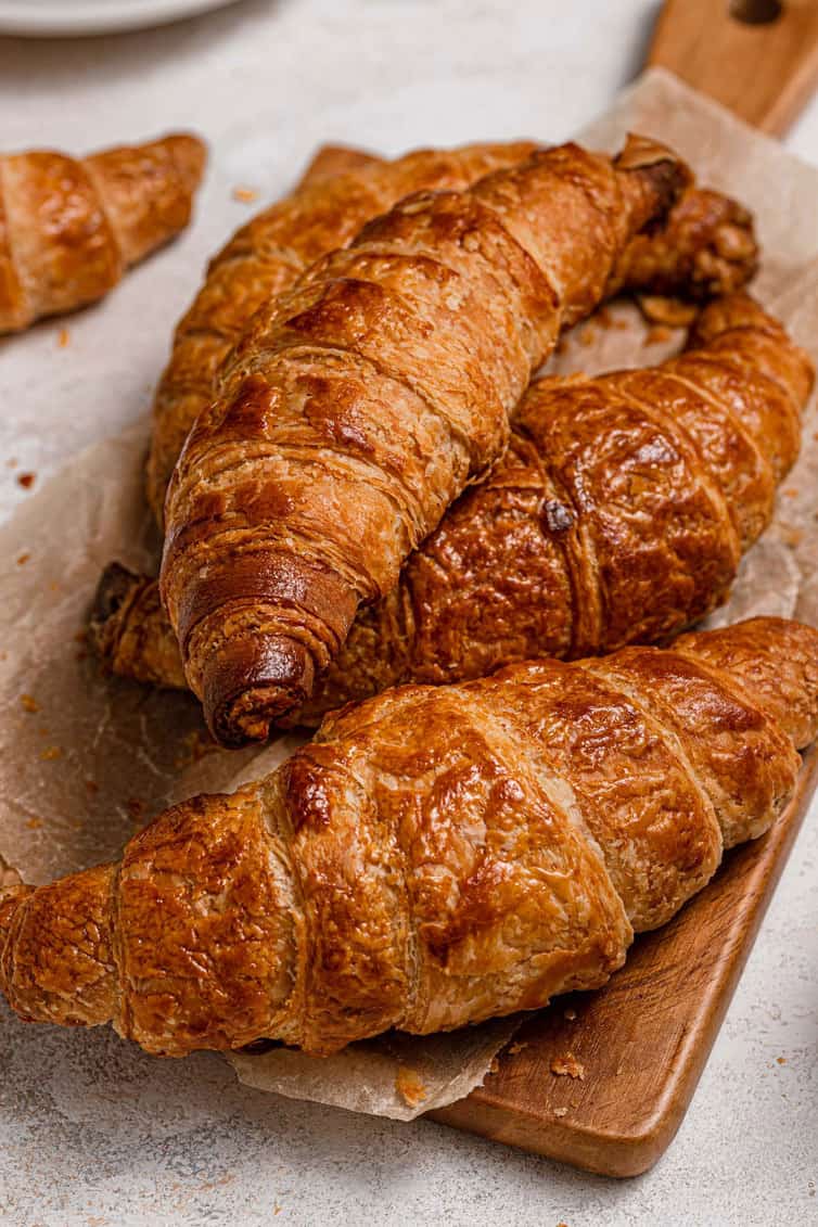 Croissants stacked together on a wooden cutting board.