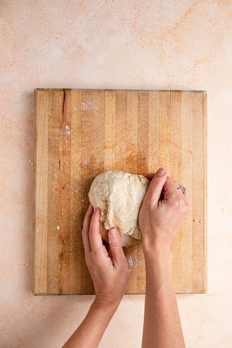 Two hands kneading dough on a wooden board.