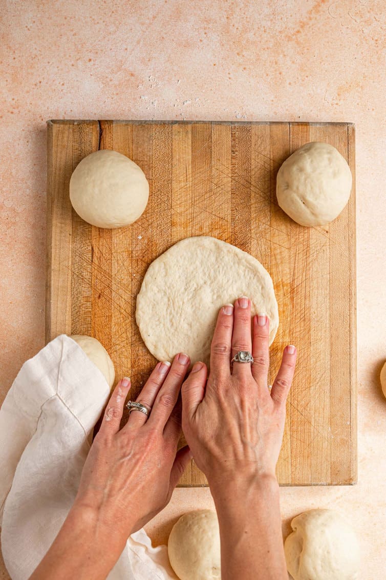 Shaping pita dough into a flat circle.