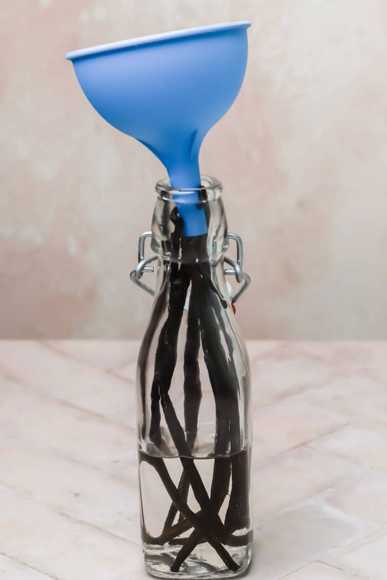Glass bottle with vanilla beans inside and a funnel in the top.
