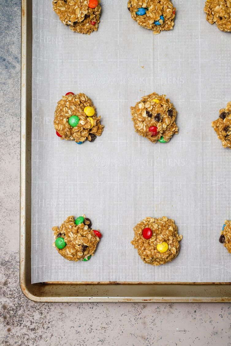Balls of monster cookie dough on parchment lined baking sheet.