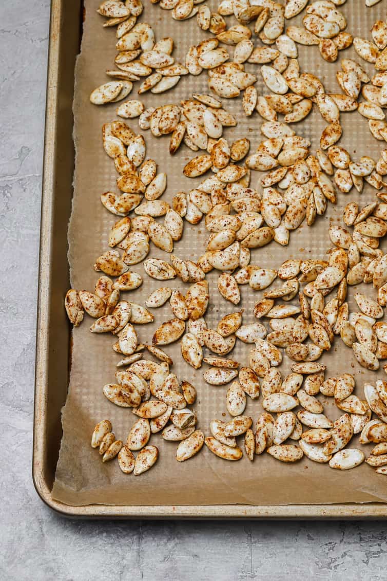 Seasoned pumpkin seeds spread out on a baking sheet.