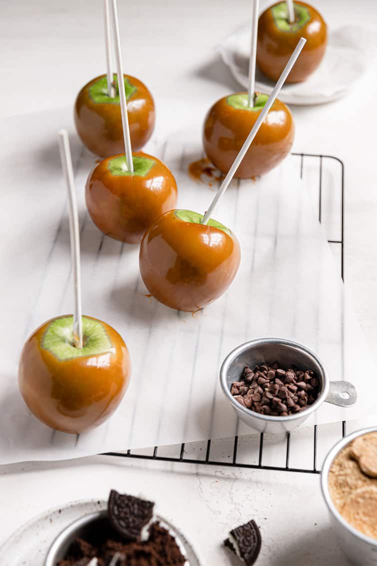 Caramel-coated apples on parchment paper on a wire rack.