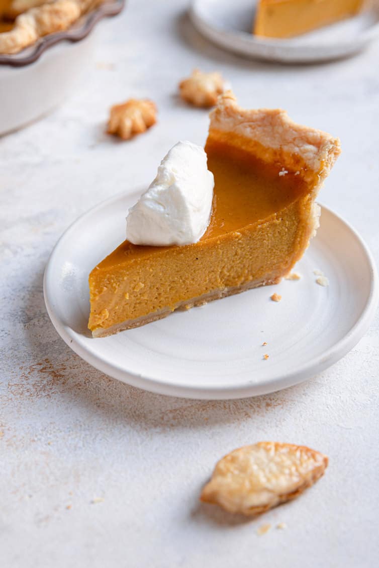 Slice of pumpkin pie on a plate with whipped cream on top.