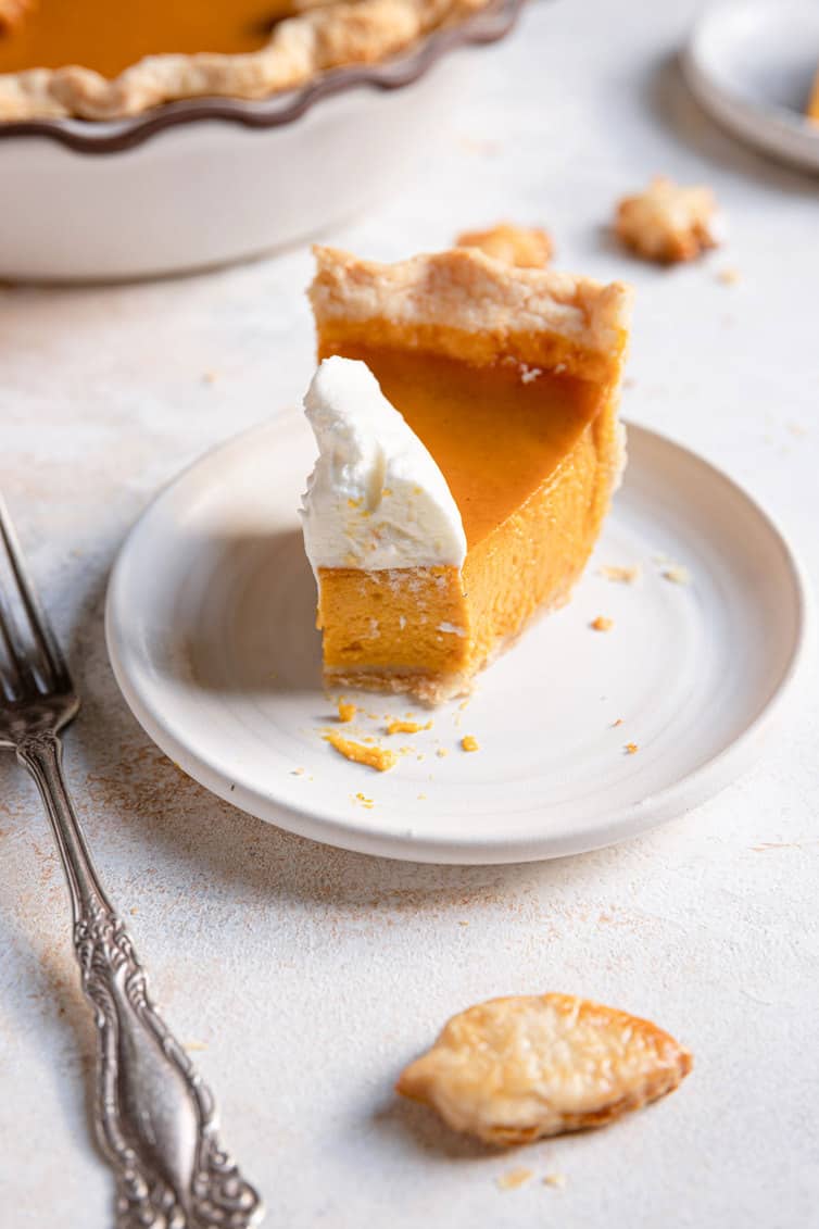 A slice of pumpkin pie with whipped cream and a forkful taken out of it.