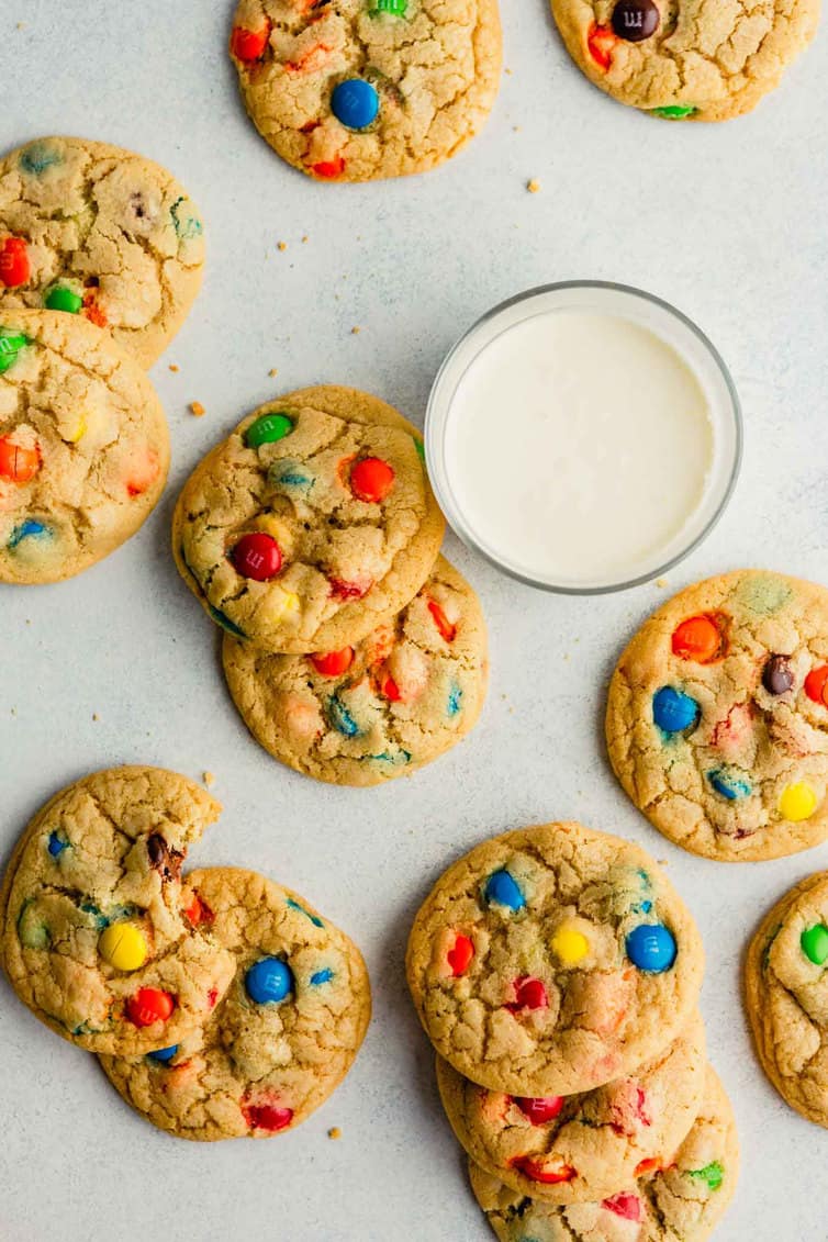 An overhead photo of M&M cookies on counter with a glass of milk.