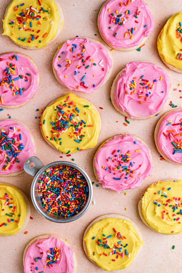 Pink and yellow frosted Lofthouse Cookies with a bowl of rainbow sprinkles.