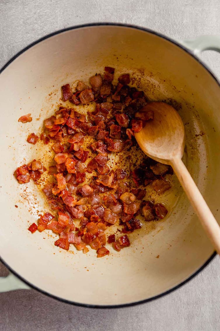 Bacon being fried in a white Dutch oven.