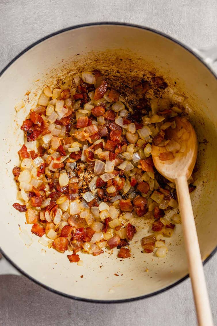 Sauteeing bacon and onion in a white Dutch oven.