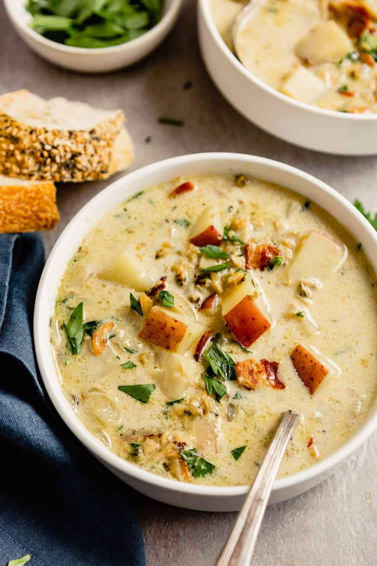 Bowl of New England clam chowder with bread and salad in the background.