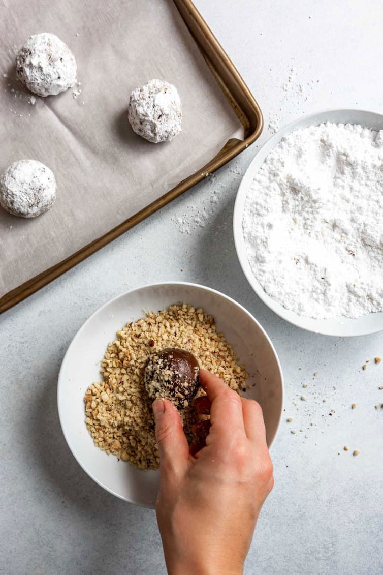 Rolling ball of Nutella cookie dough in chopped hazelnuts.