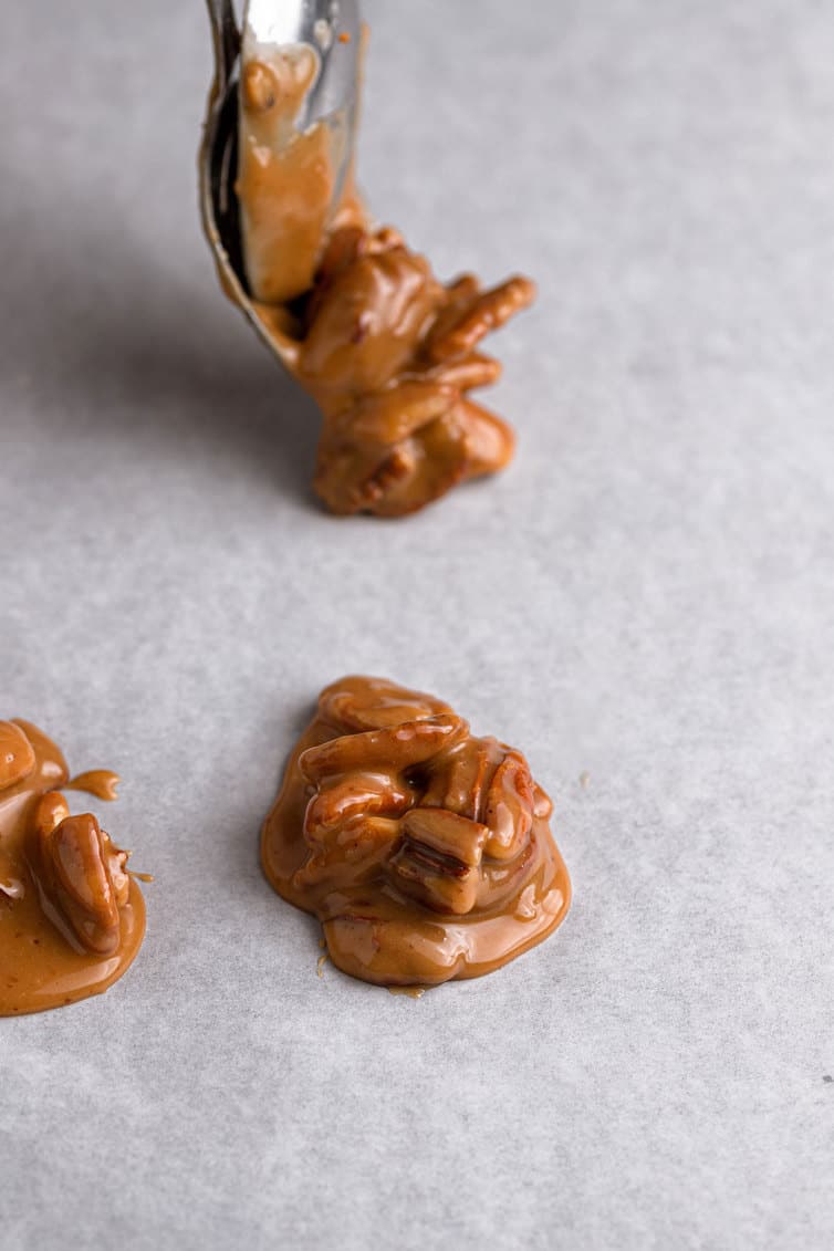 Spooning scoops of pecan pralines onto parchment paper.