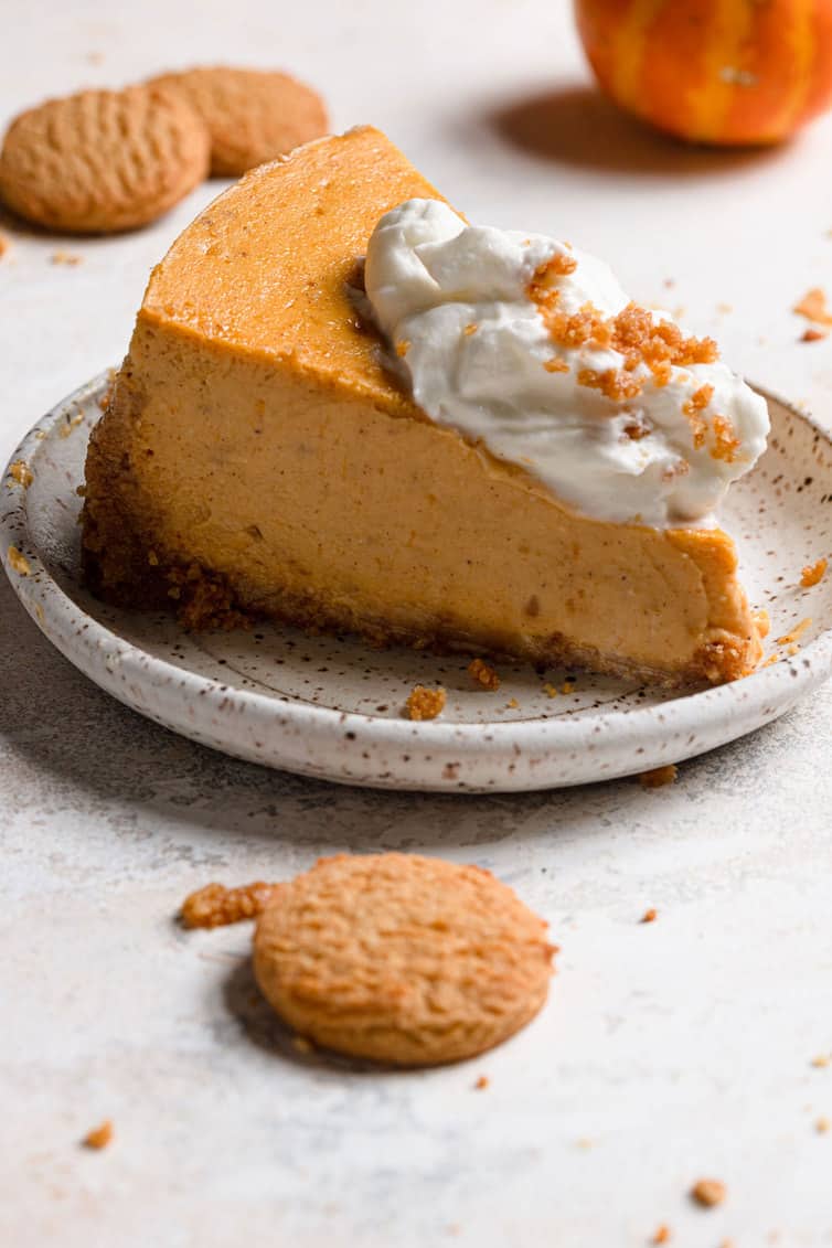 Slice of pumpkin cheesecake on plate topped with whipped cream.