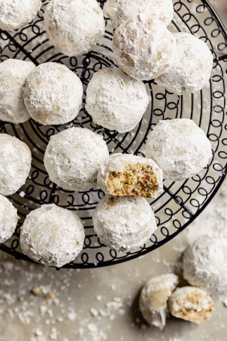Snowball cookies on wire rack with one half eaten.