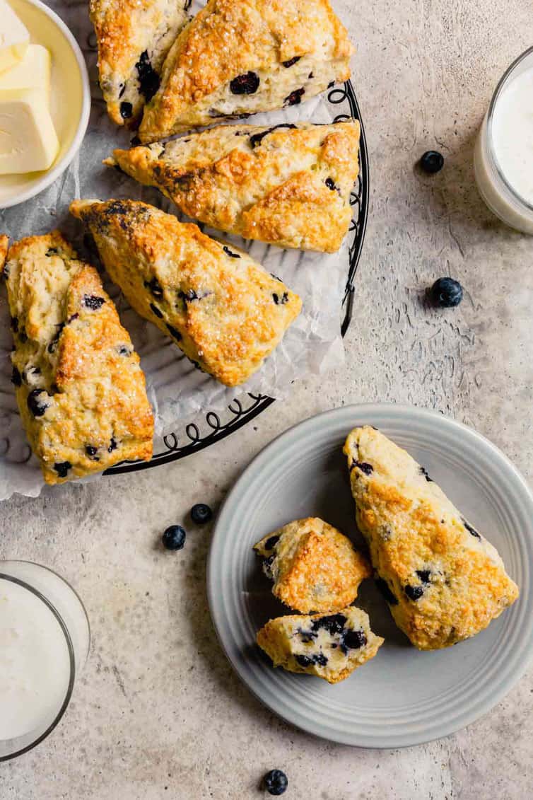 Two baked buttermilk scones on a plate at the bottom right and four baked buttermilk scones in the top left on a cooling rack covered in parchment paper.