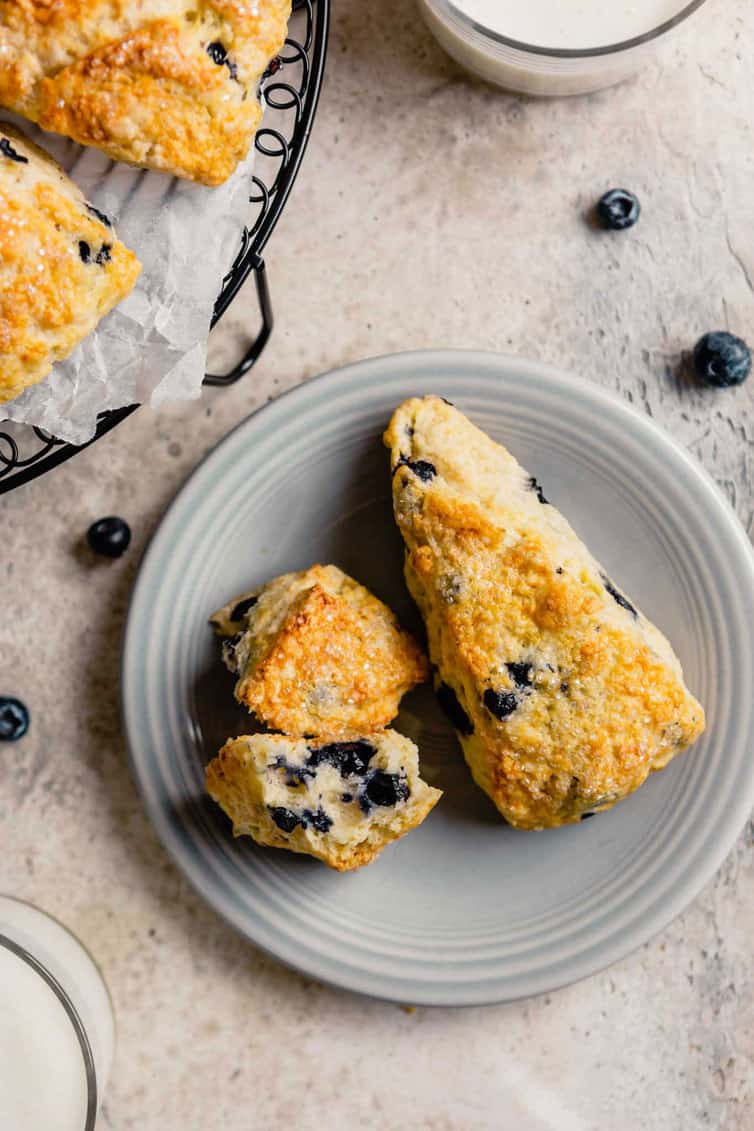 A light grey plate with two buttermilk scones on a counter with a few fresh blueberries.