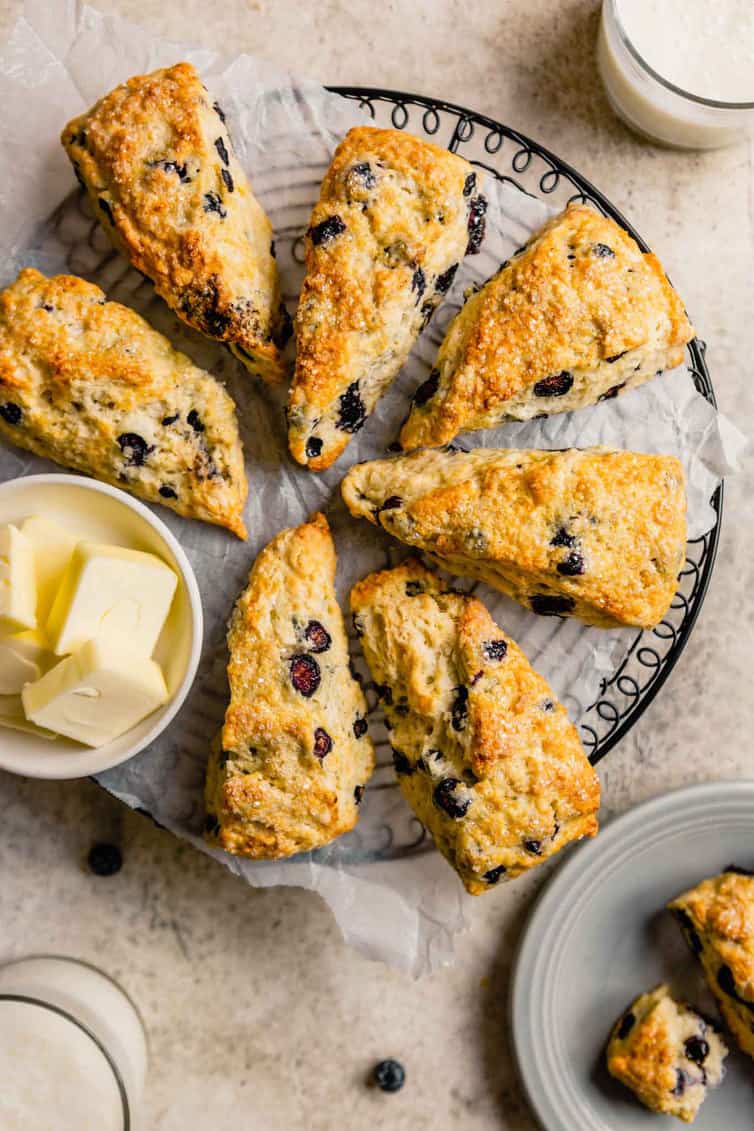 A black wire cooling rack covered in parchment paper with buttermilk scones on top with a small bowl with butter to the left of the cooling rack.