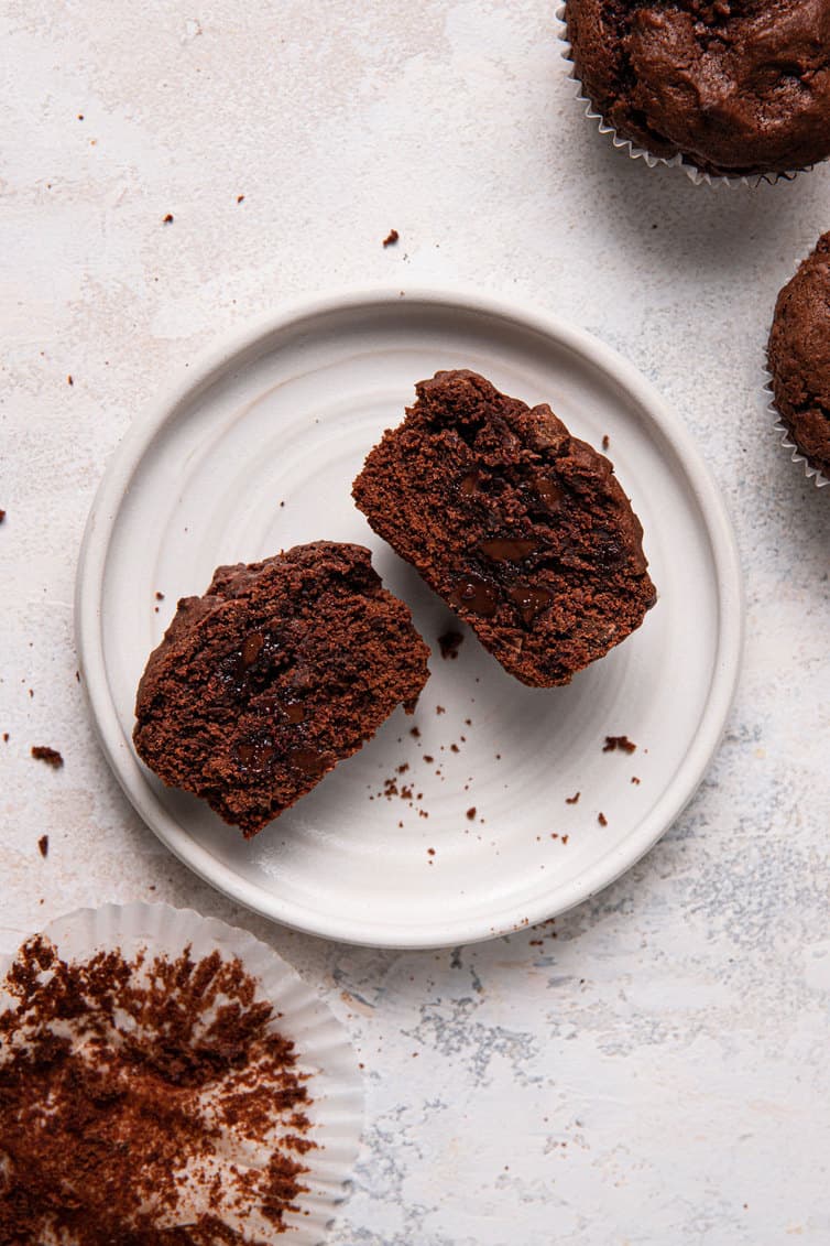 A chocolate muffin cut in half on a white plate.