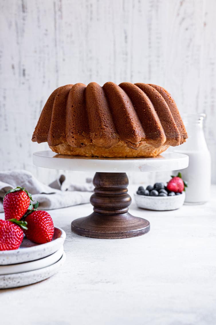 Cream cheese pound cake on a pedestal stand with strawberries in a bowl.