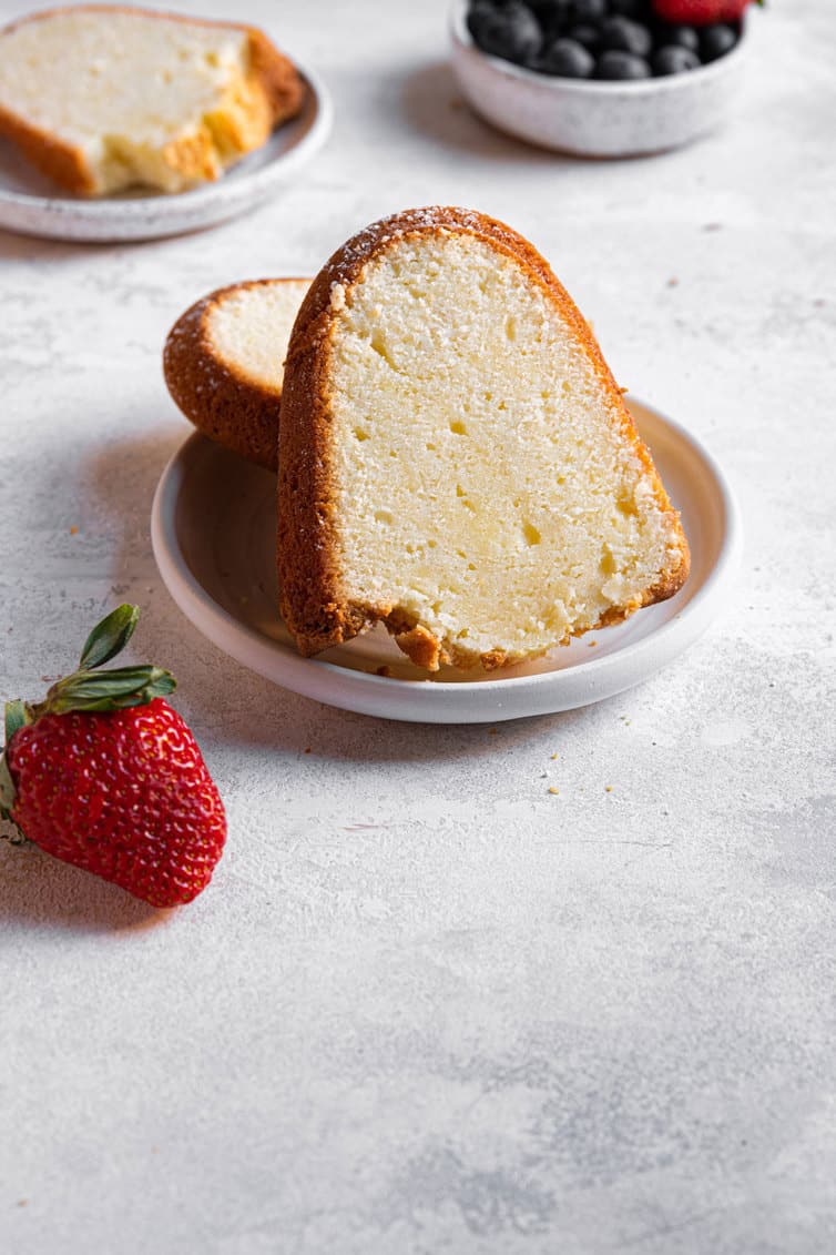 A slice of cream cheese pound cake on a plate with a strawberry next to it.