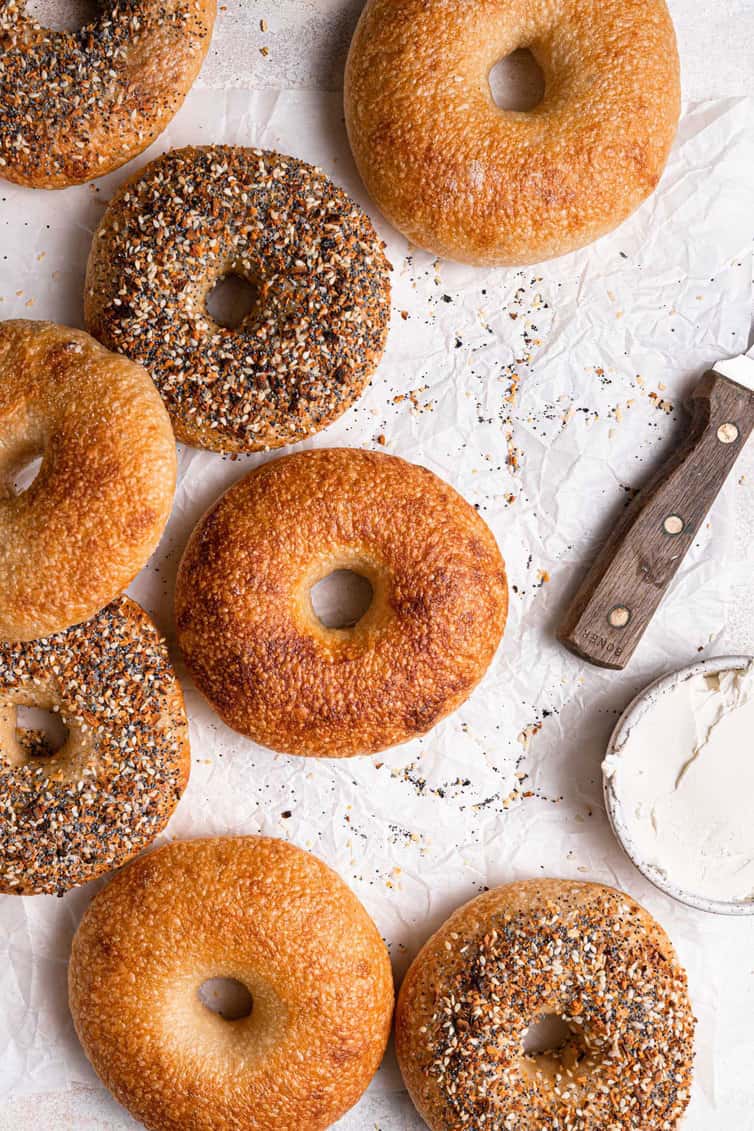 Homemade bagels on a counter with a knife and cream cheese.