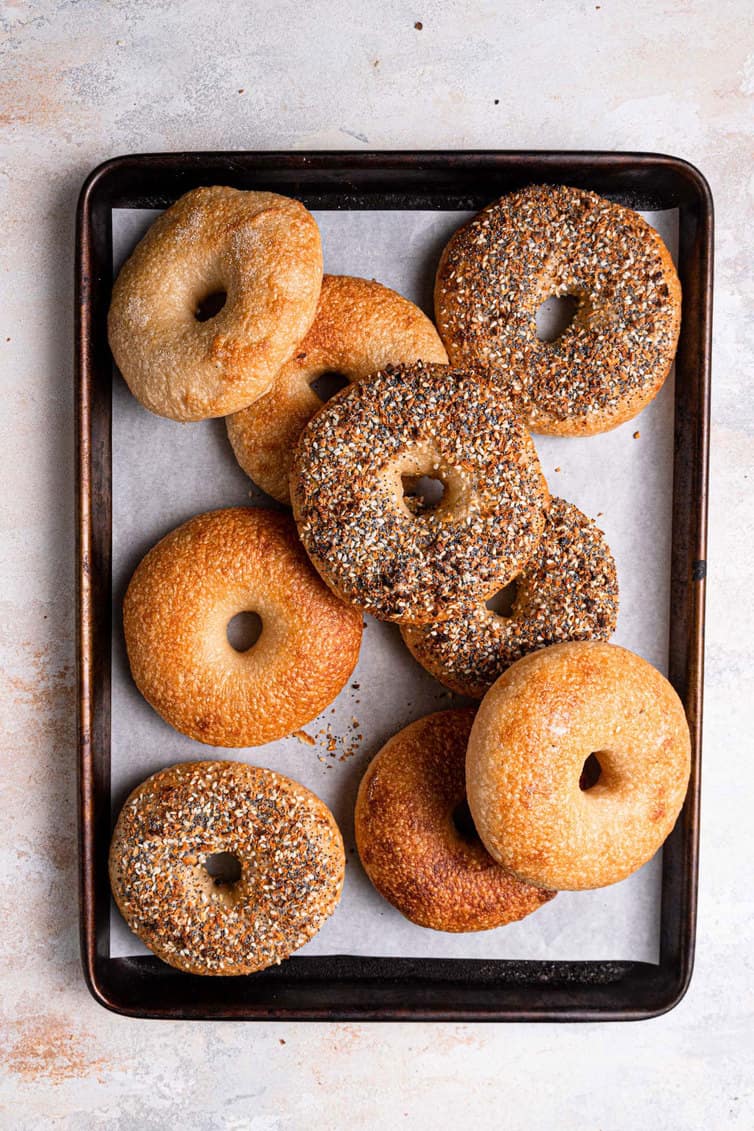 Plain and everything bagels on a baking sheet lined with parchment paper.