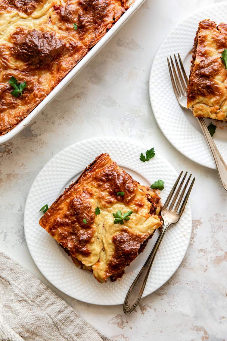 Pieces of moussaka on white plates with baking dish in background.