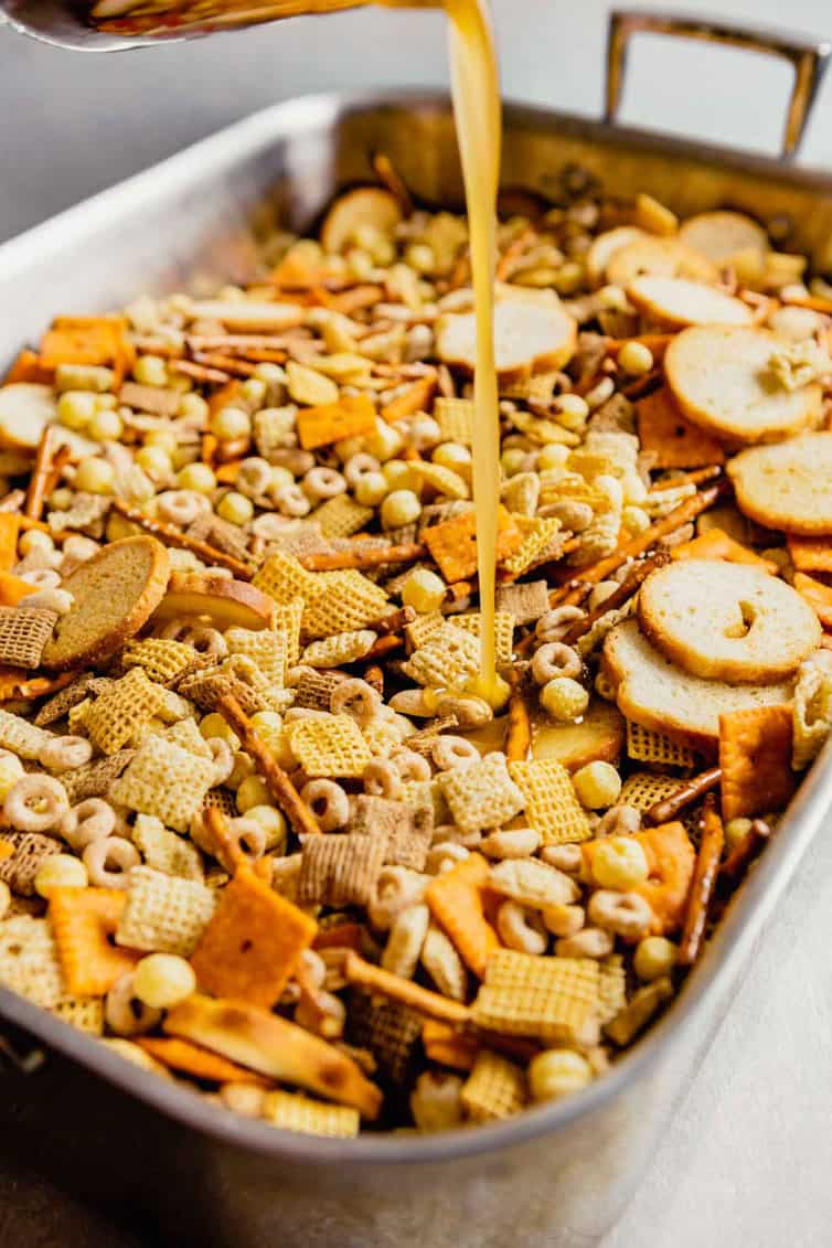 Pouring melted butter and bacon drippings over nuts and bolts mixture.