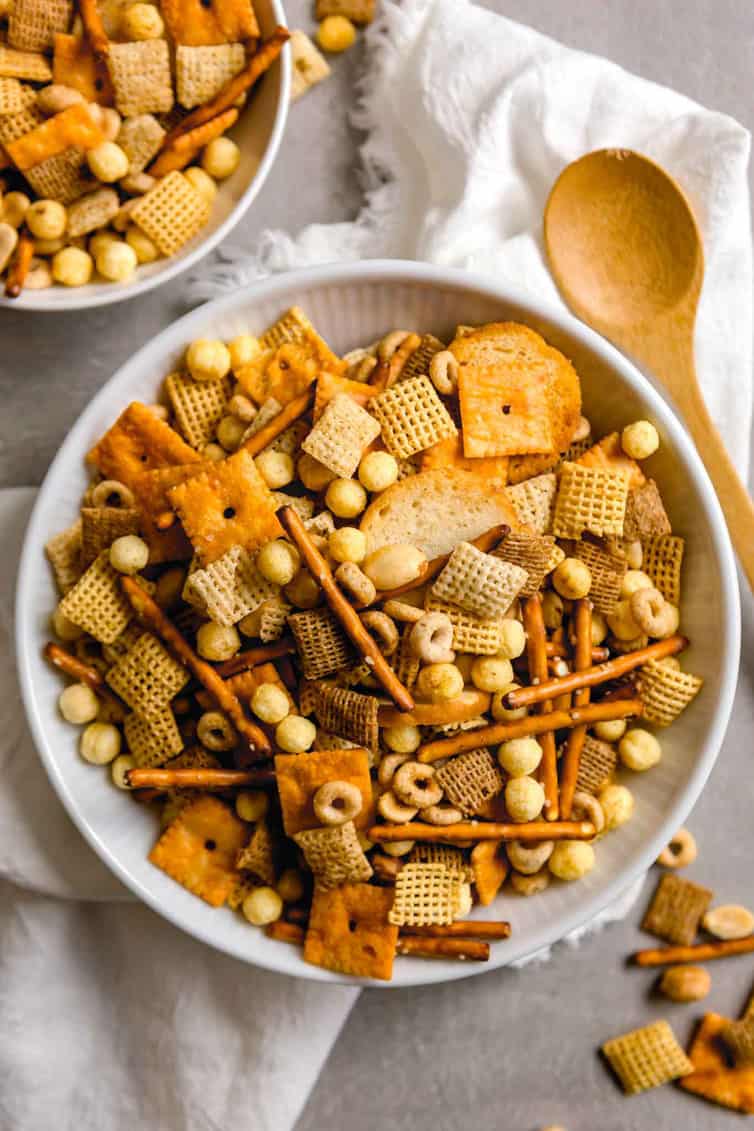 A bowl of nuts and bolts snack mix with wooden spoon.