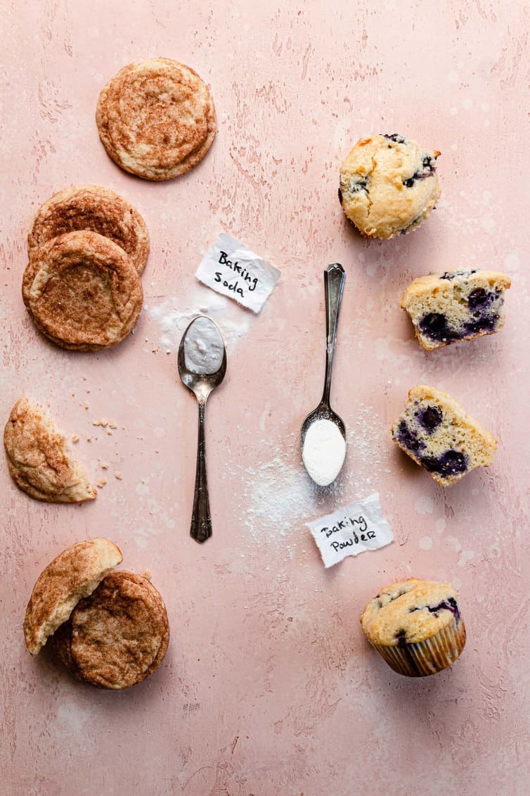 Snickerdoodle cookies and blueberry muffins with spoonfuls of baking soda and baking powder next to them.