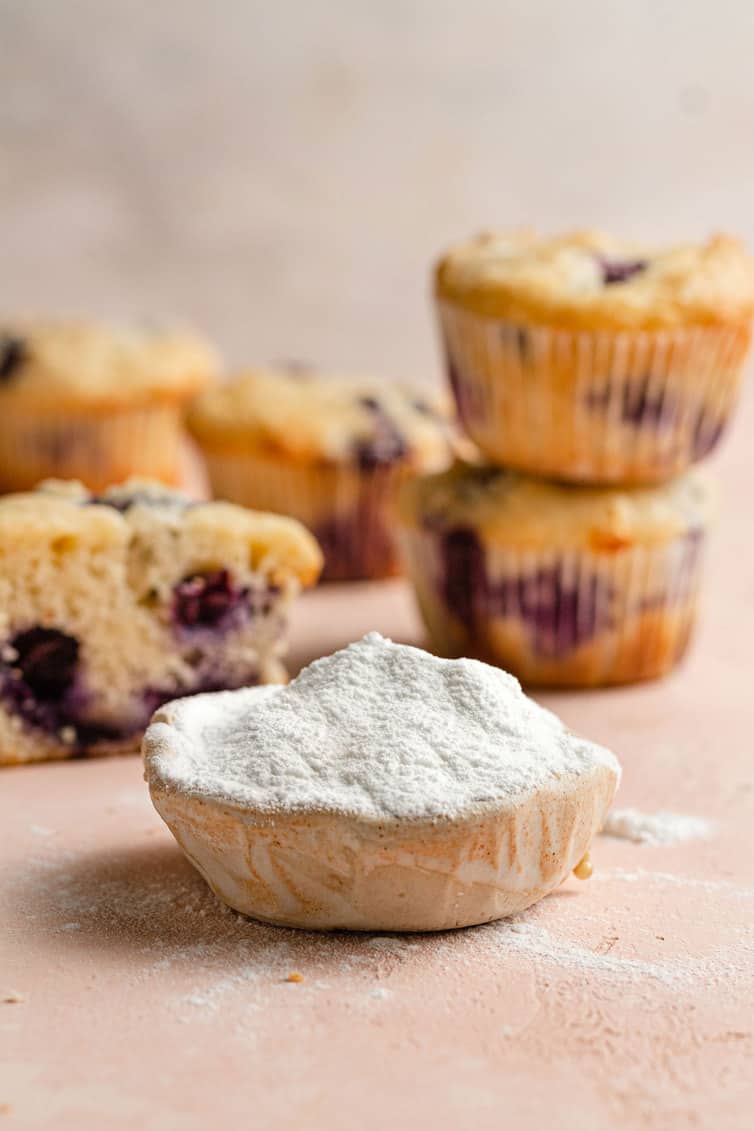 A scoop of baking powder in front of blueberry muffins.