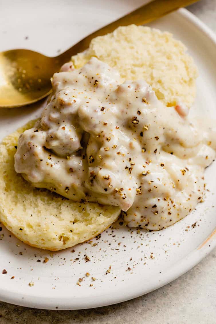 A top down picture of biscuits and gravy on a white plate with a gold spoon in the back.