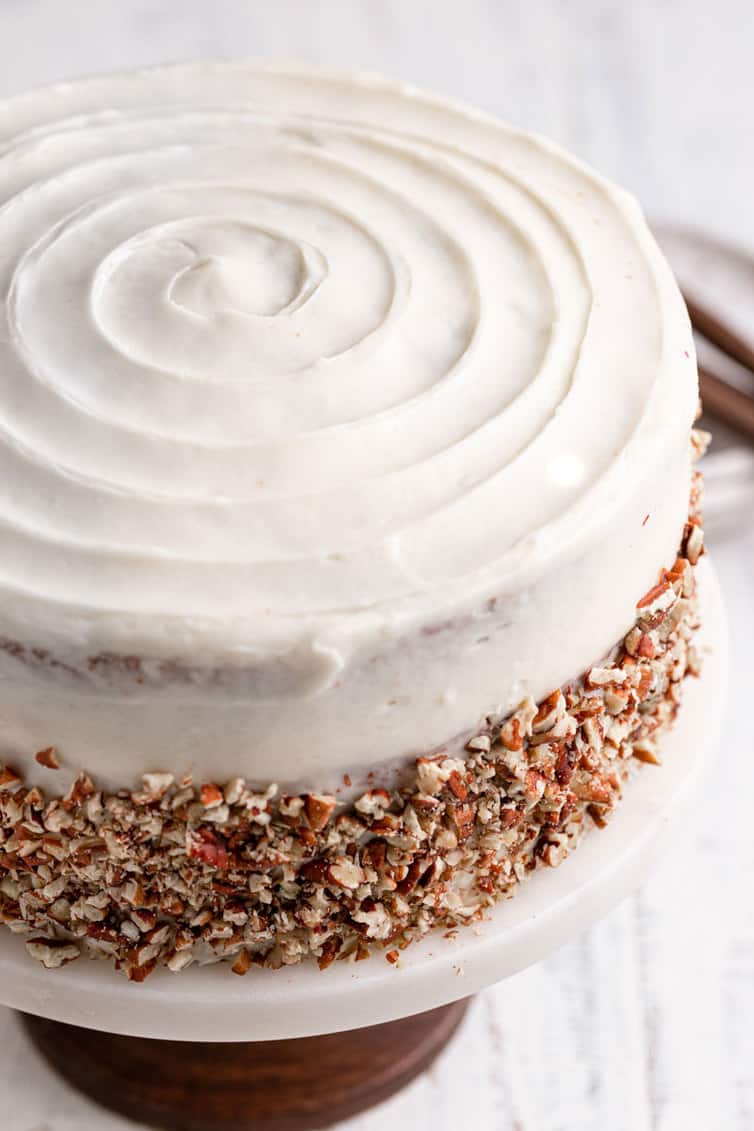 Fully assembled carrot cake with spiral icing design on top and pecans pressed into sides.