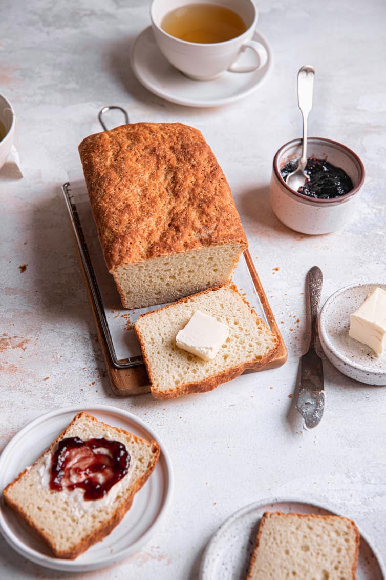 English muffin bread sliced on plates with jam on one slice and a slab of butter on another slice.