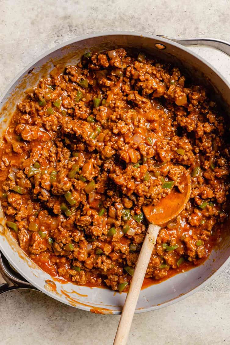 Homemade sloppy joe meat in a skillet with a wooden spoon.