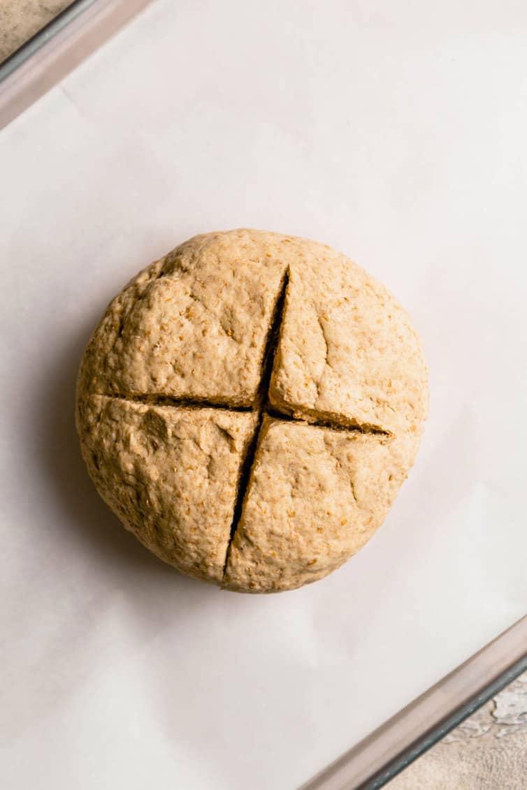 Irish brown bread dough on a parchment paper lined baking sheet with a cross cut in the top of the loaf.
