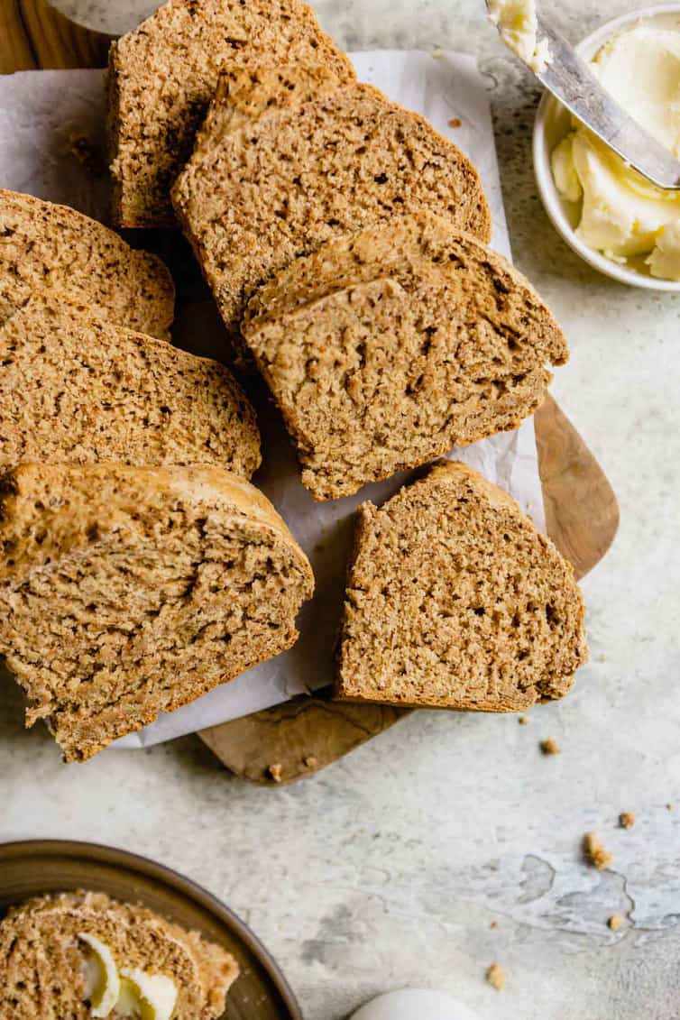 Sliced Irish brown bread on a wooden cutting board with a small bowl of butter to the right.