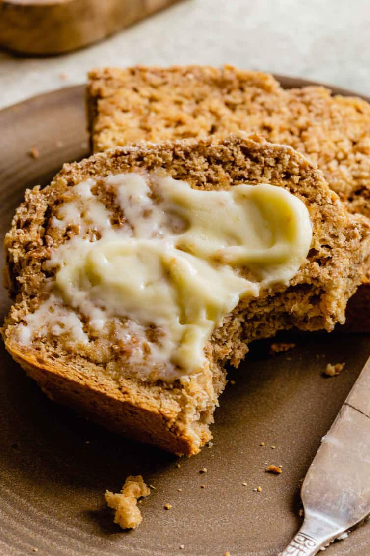 A slice of Irish brown bread slathered with butter on a wooden cutting board.