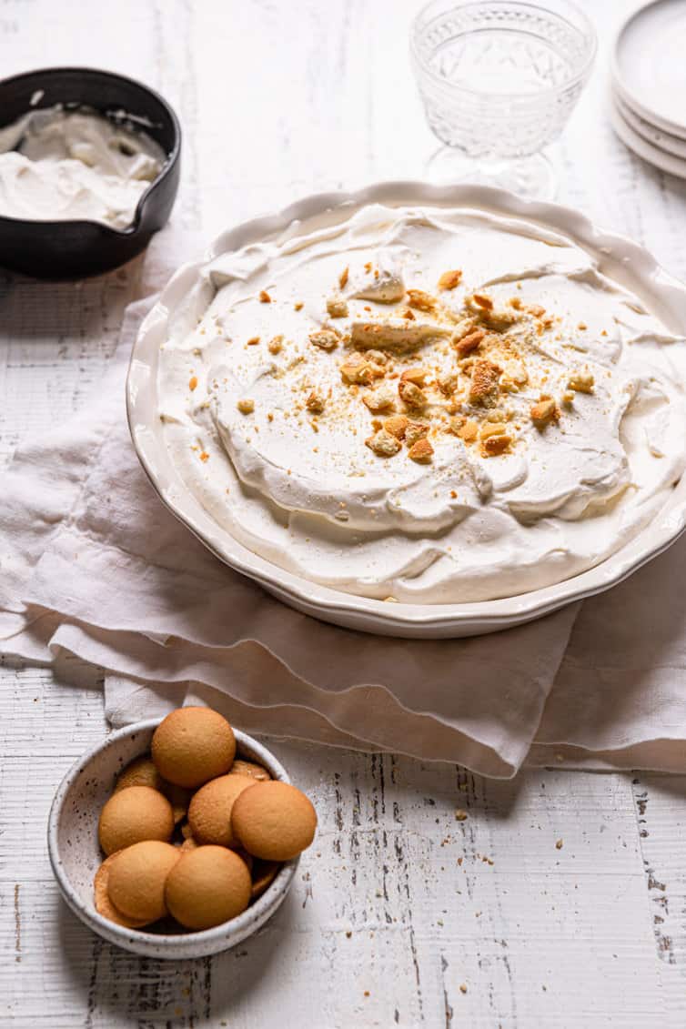 A pie pan with homemade banana pudding on a towel with a bowl of eggs in the front left.