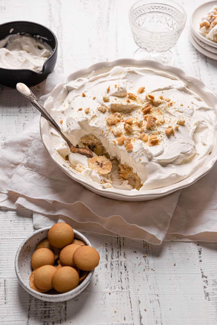 A spoon with a scoop of banana pudding in a pie pan with a small bowl of eggs in the bottom left.