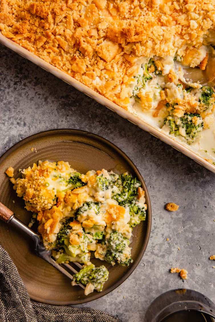 A top down picture of broccoli casserole on a brown plate with a fork to the left and a casserole dish to the right.