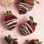 Chocolate strawberries drizzled with white chocolate on a pink counter.