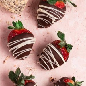 Chocolate strawberries drizzled with white chocolate on a pink counter.