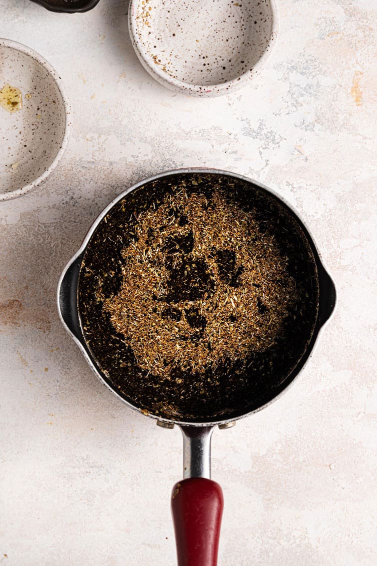 Herb oil for focaccia in a sauce pan on a white counter.