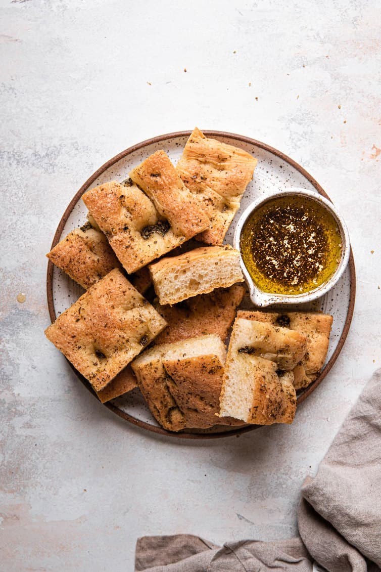A top down photo of a small plate with a brown rim filled with a pile of sliced focaccia and a small herb oil bowl to the right.