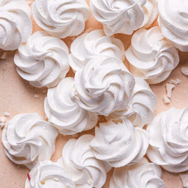 A top down photo of a pile of white meringue cookies with one on the top in the center.